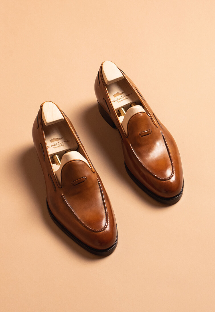 A pair of handmade brown leather shoes with a sleek design and wooden shoe trees inside.
