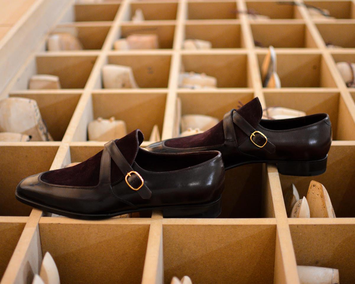 A pair of dark brown leather shoes with a burgundy suede panel and a gold buckle detail.