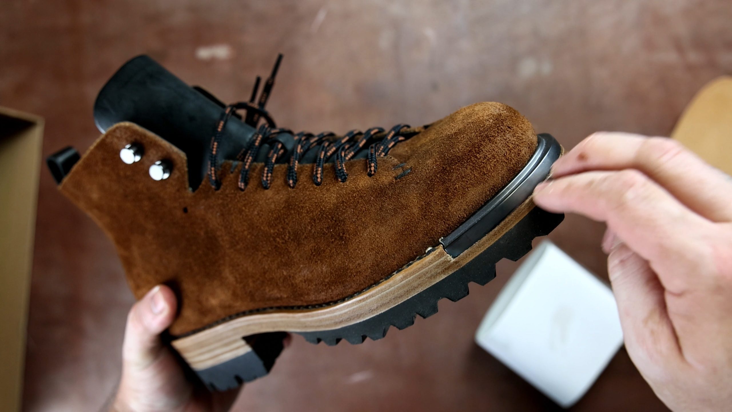 A close-up of a brown suede FEIT wholecut hiking boot being examined, highlighting its textured surface and sturdy sole.