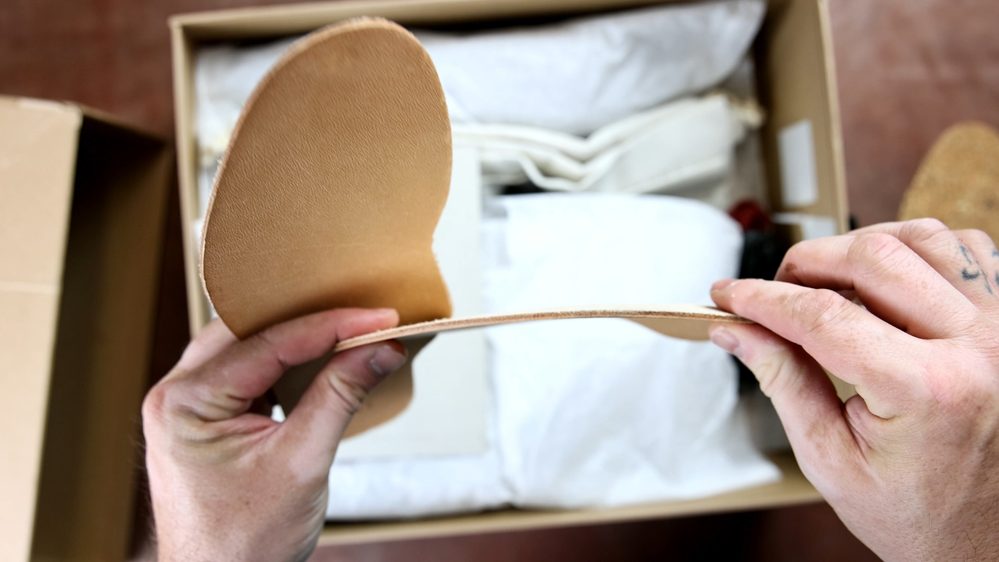 A person holds a tan leather insole for the FEIT wholecut hiking boots.