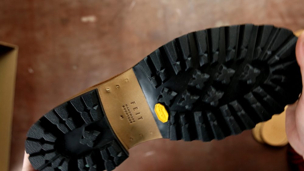 The image shows the black rubber sole of FEIT wholecut hiking boots, featuring a textured pattern and a yellow Vibram logo.