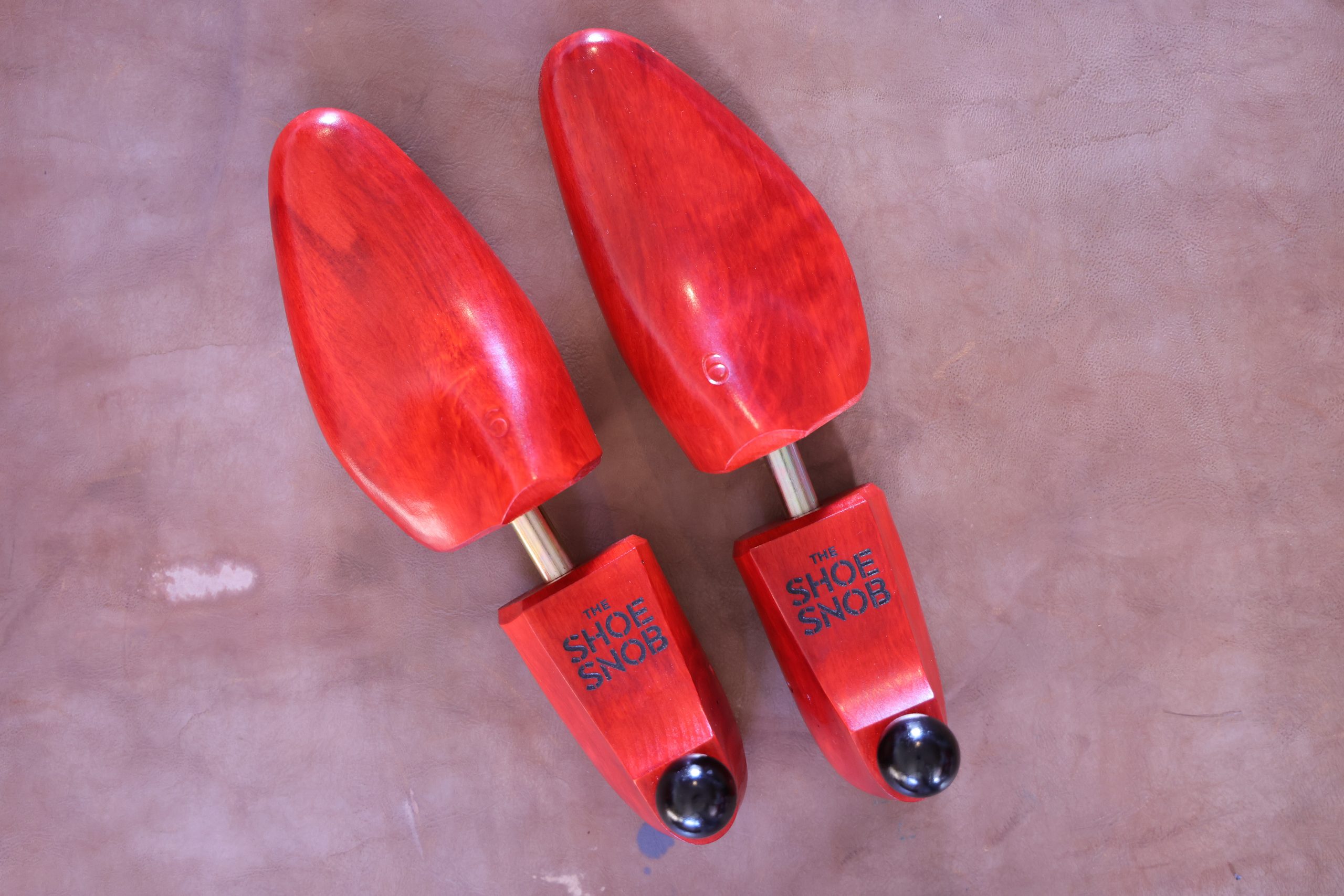 A pair of red wooden shoe trees with a black ball at the end, demonstrating how to properly store dress shoes.