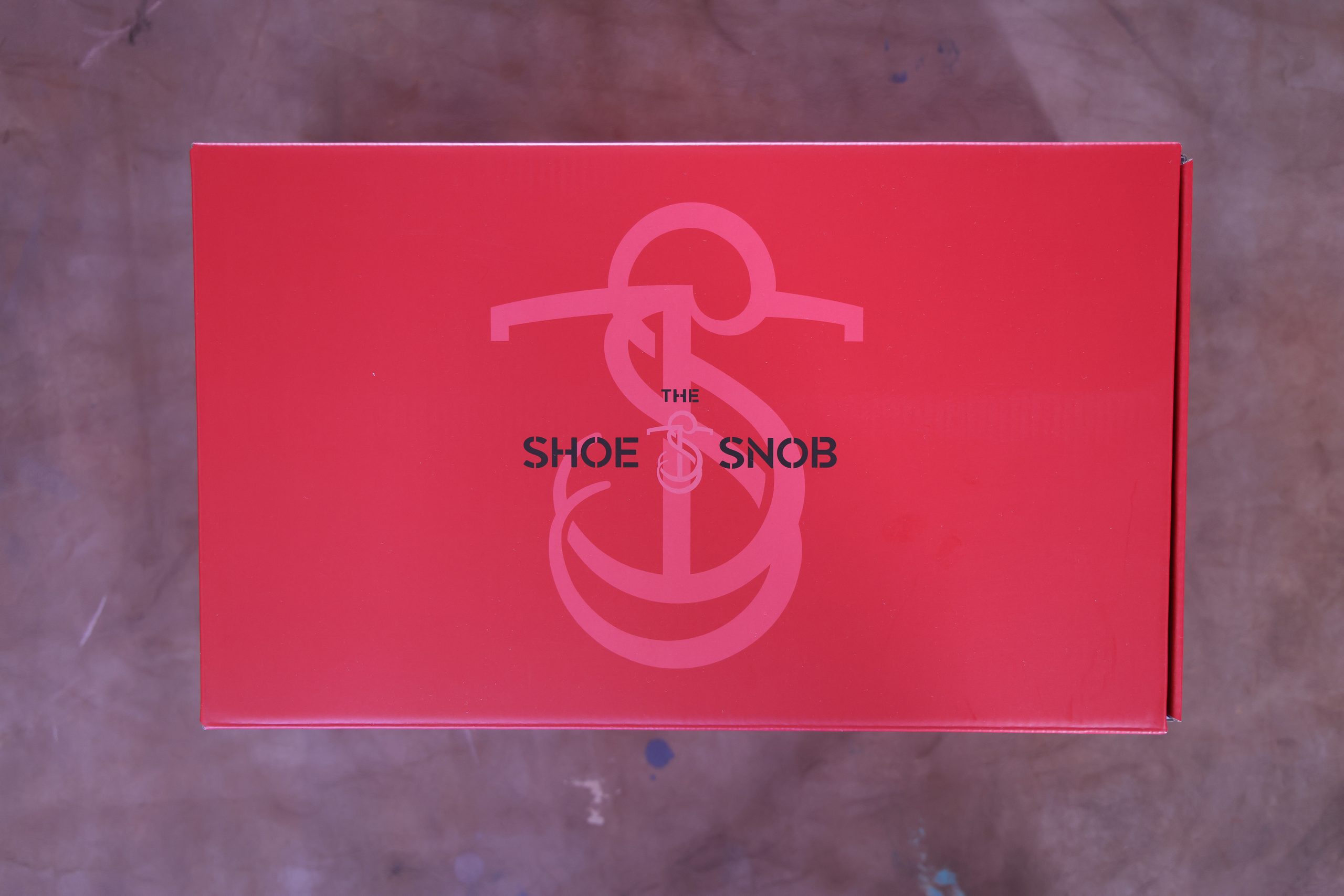 A red shoe box with the text "THE SHOE SNOB" prominently displayed, illustrating how to properly store dress shoes.