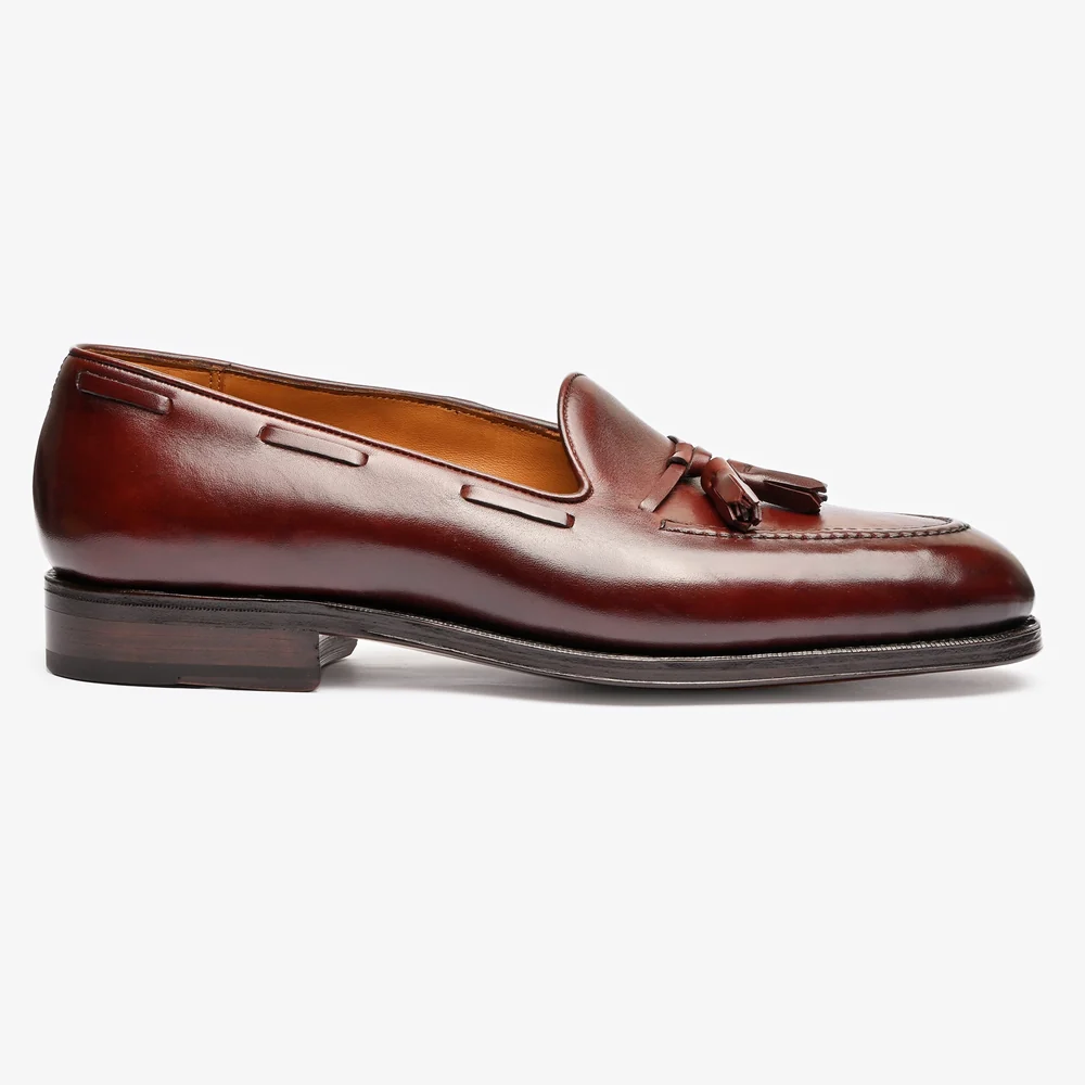 A burgundy leather loafer with a tassel detail and a wooden heel.