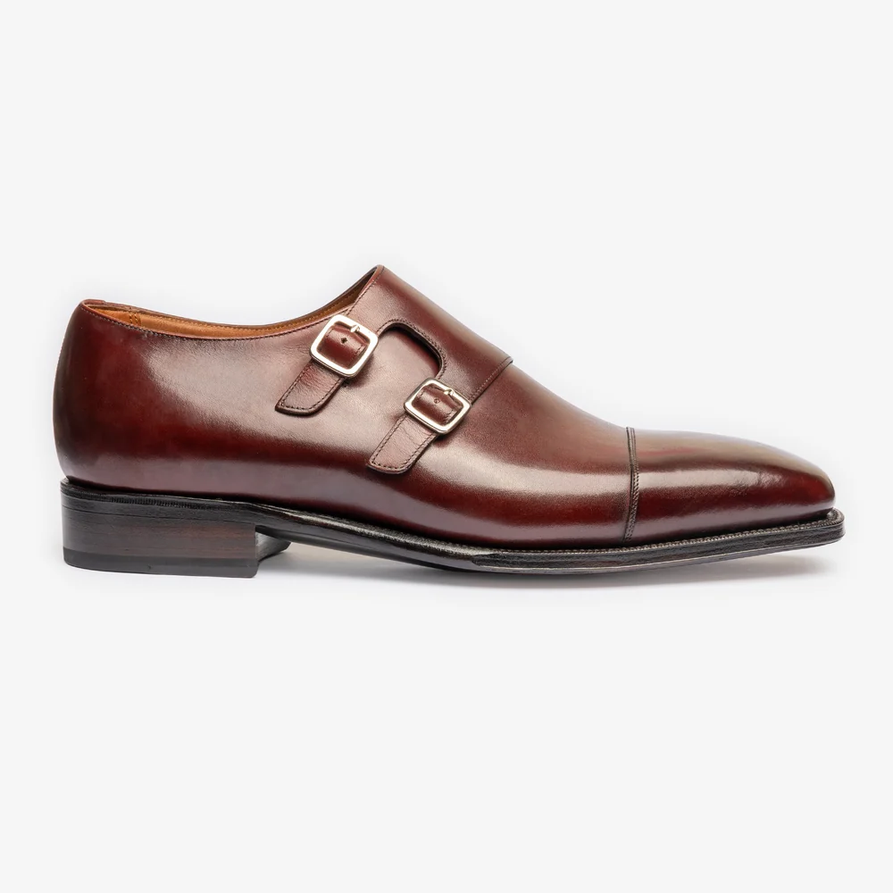 A side view of a polished burgundy leather shoe featuring two silver buckles.