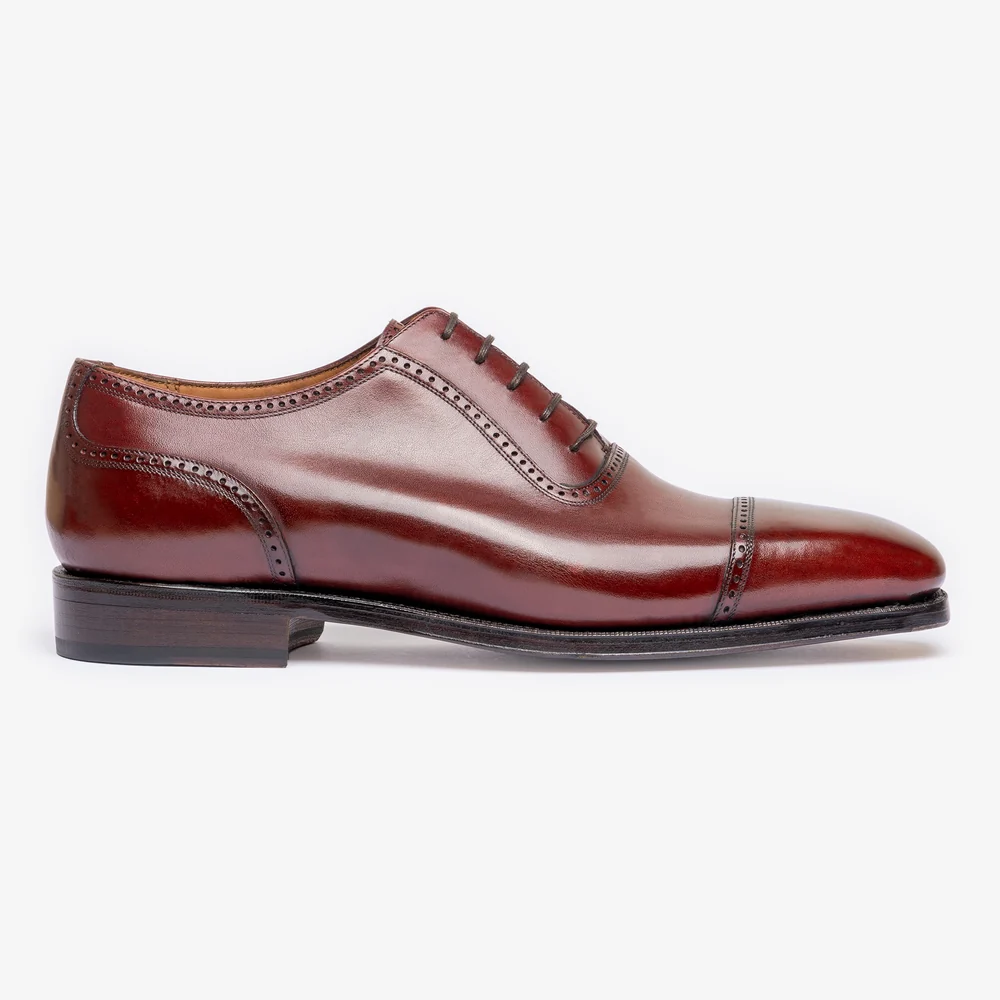 A side view of a polished burgundy leather dress shoe with a cap toe and decorative perforations.