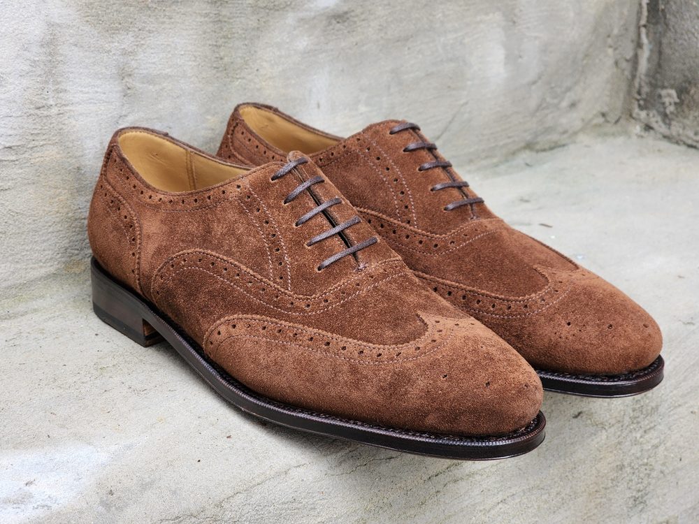 A pair of brown suede brogue shoes with decorative perforations, featured in the context of "Oxford vs wingtip."