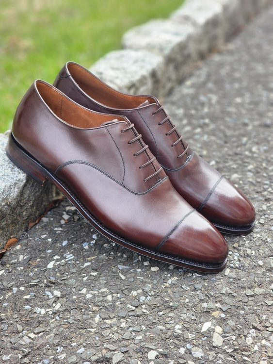 A pair of polished brown leather Oxford shoes with a cap toe design, showcasing their sleek lines and lacing.