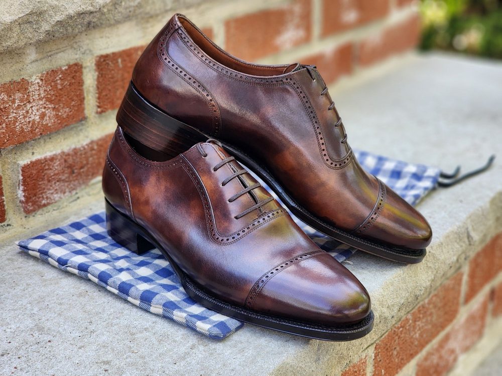 A pair of polished brown leather Oxford shoes with decorative perforations, displayed on a blue and white checkered cloth.