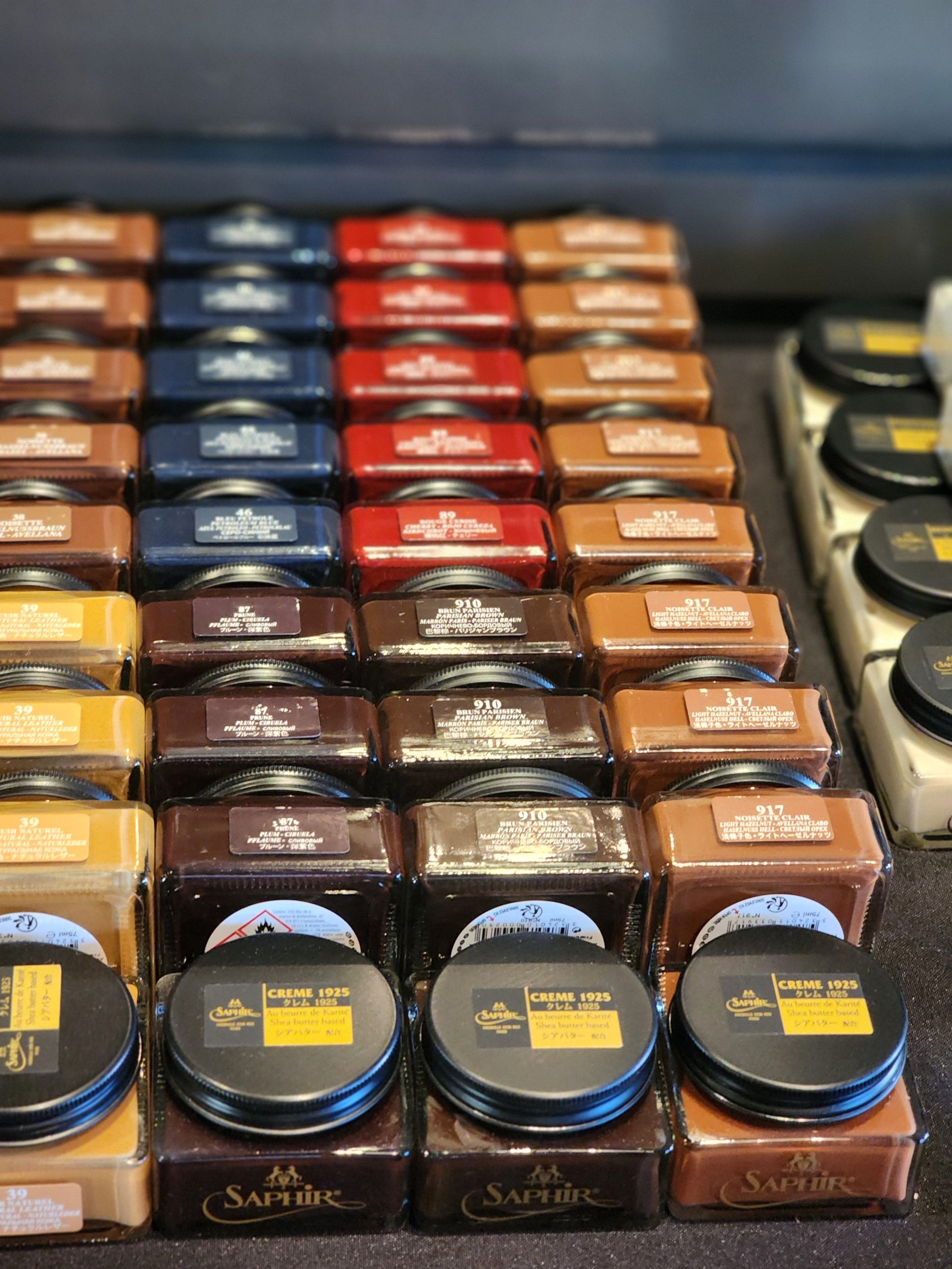 A variety of Saphir shoe cream jars in different colors, including browns, blacks, and reds on display