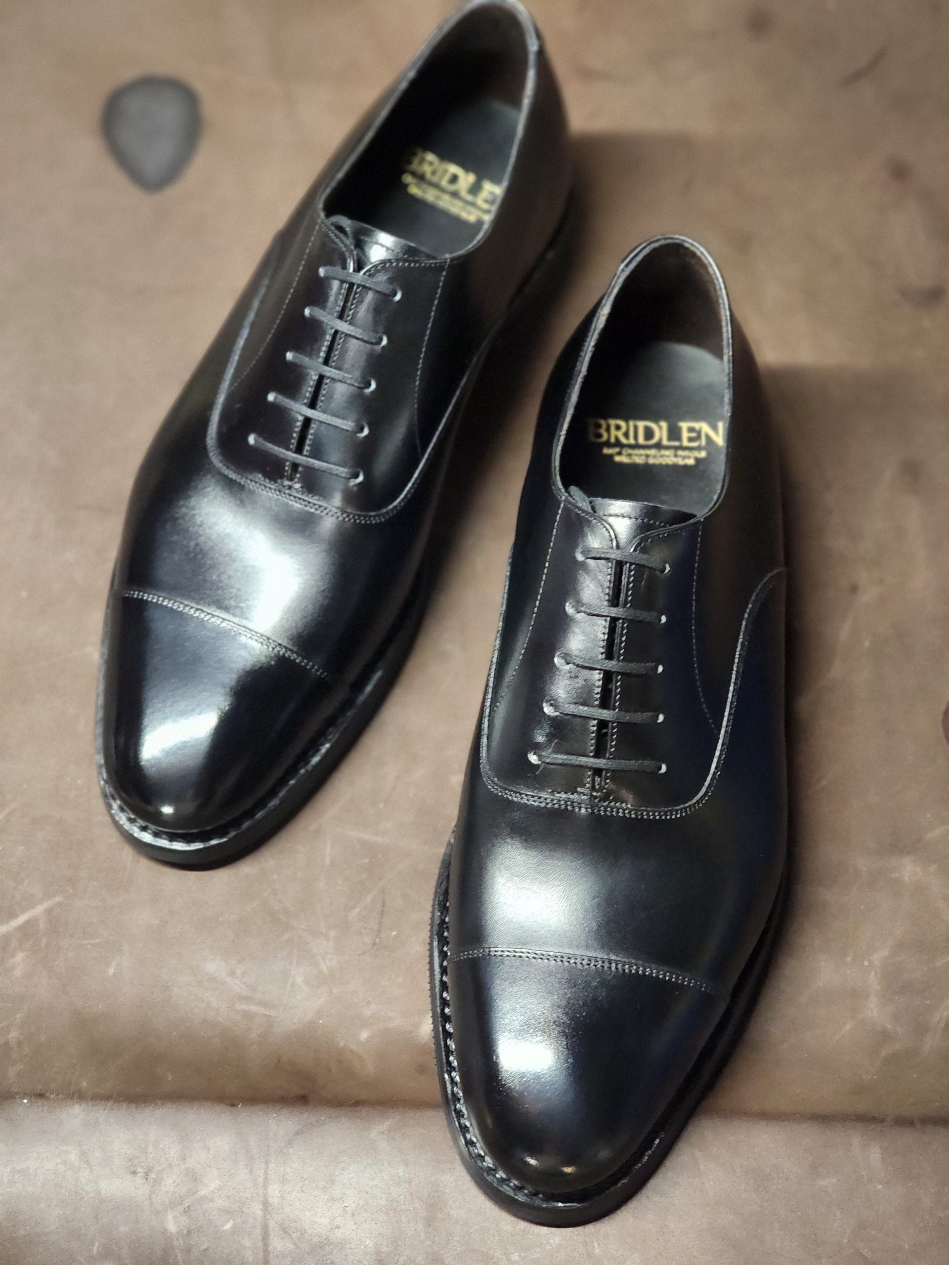A pair of polished black leather Oxford shoes with a cap toe, featuring a lace-up design.