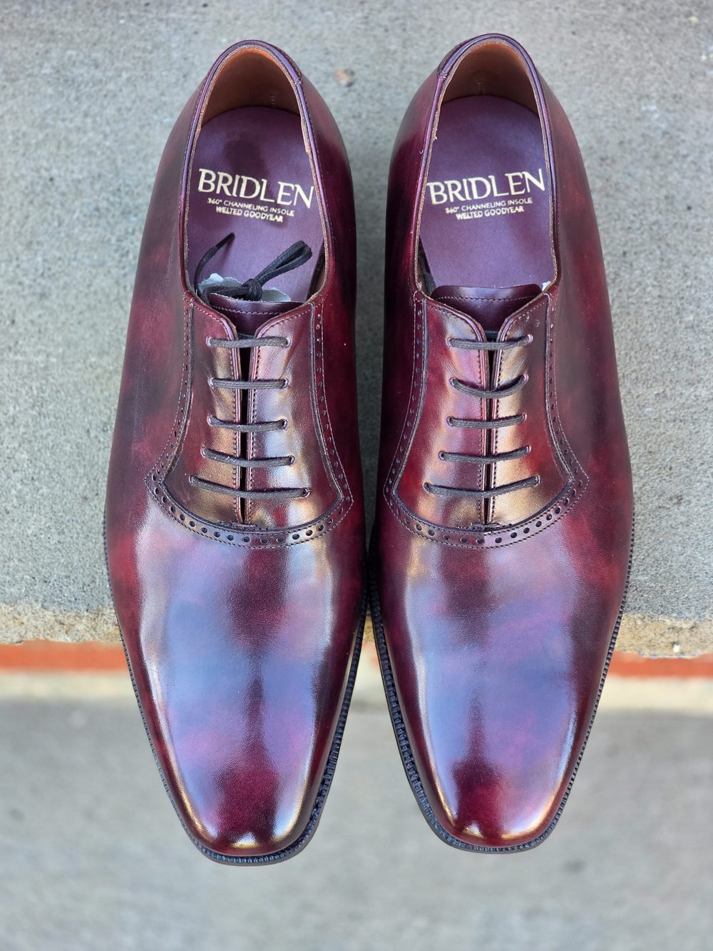 A pair of polished burgundy shoes with a classic lace-up design and decorative stitching.