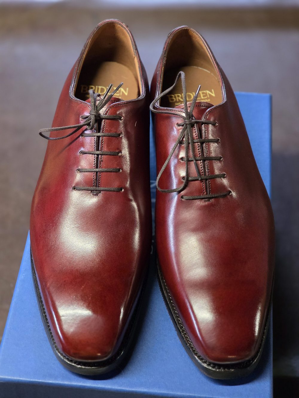 A pair of polished burgundy shoes with leather laces displayed on a blue box.