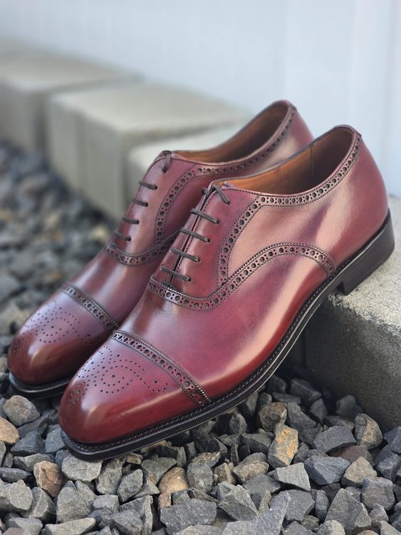 A pair of polished burgundy Oxford shoes featuring decorative perforations and laces, illustrating the Oxford vs wingtip style distinction.