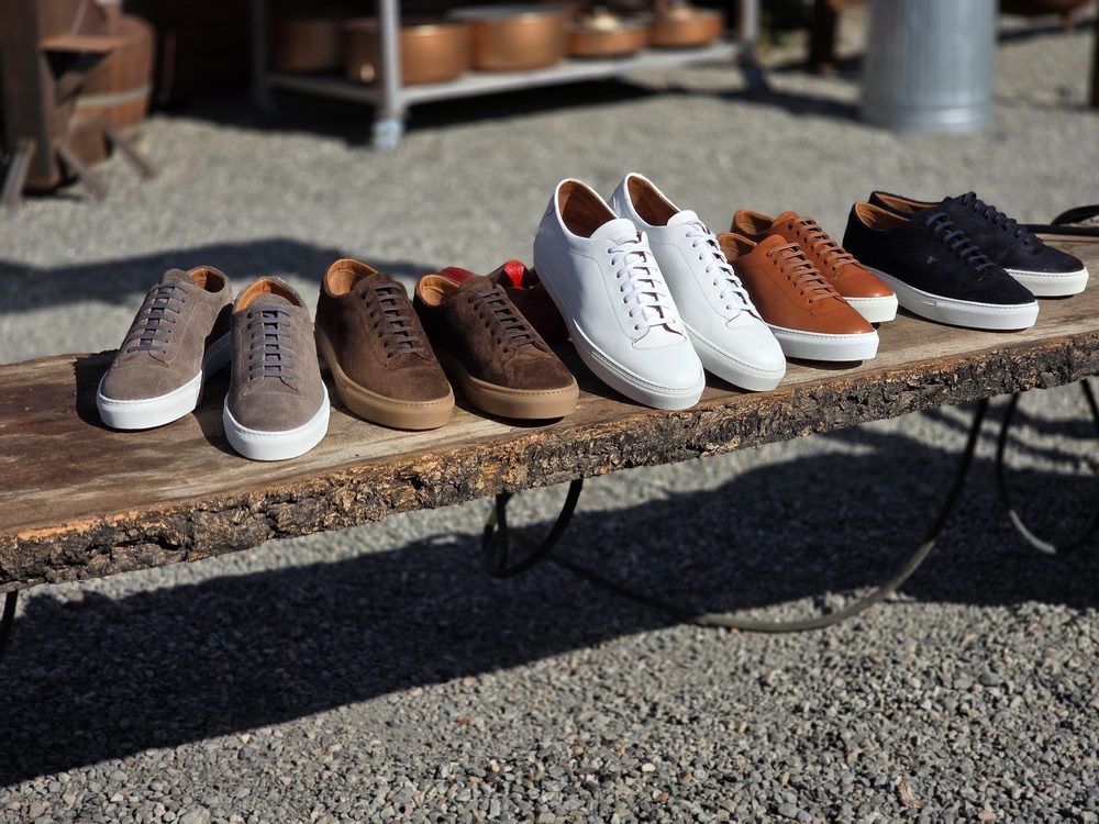 A selection of eight pairs of sneakers in various colors, including gray, brown, white, and navy, displayed on a wooden table.