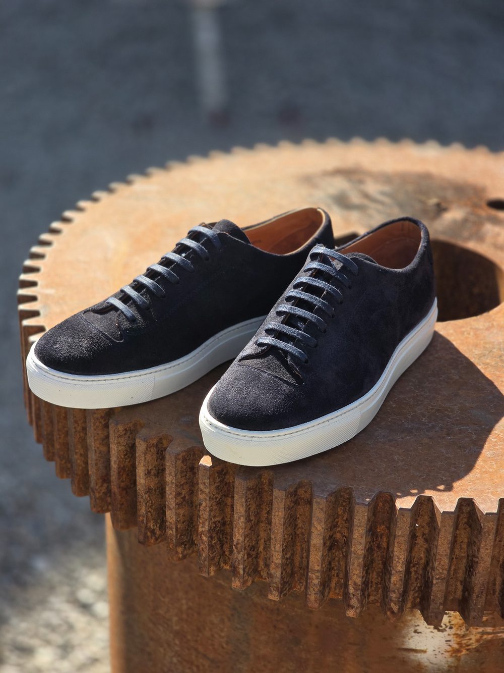 A pair of navy suede sneakers with white soles and laces, positioned on a textured metal surface.