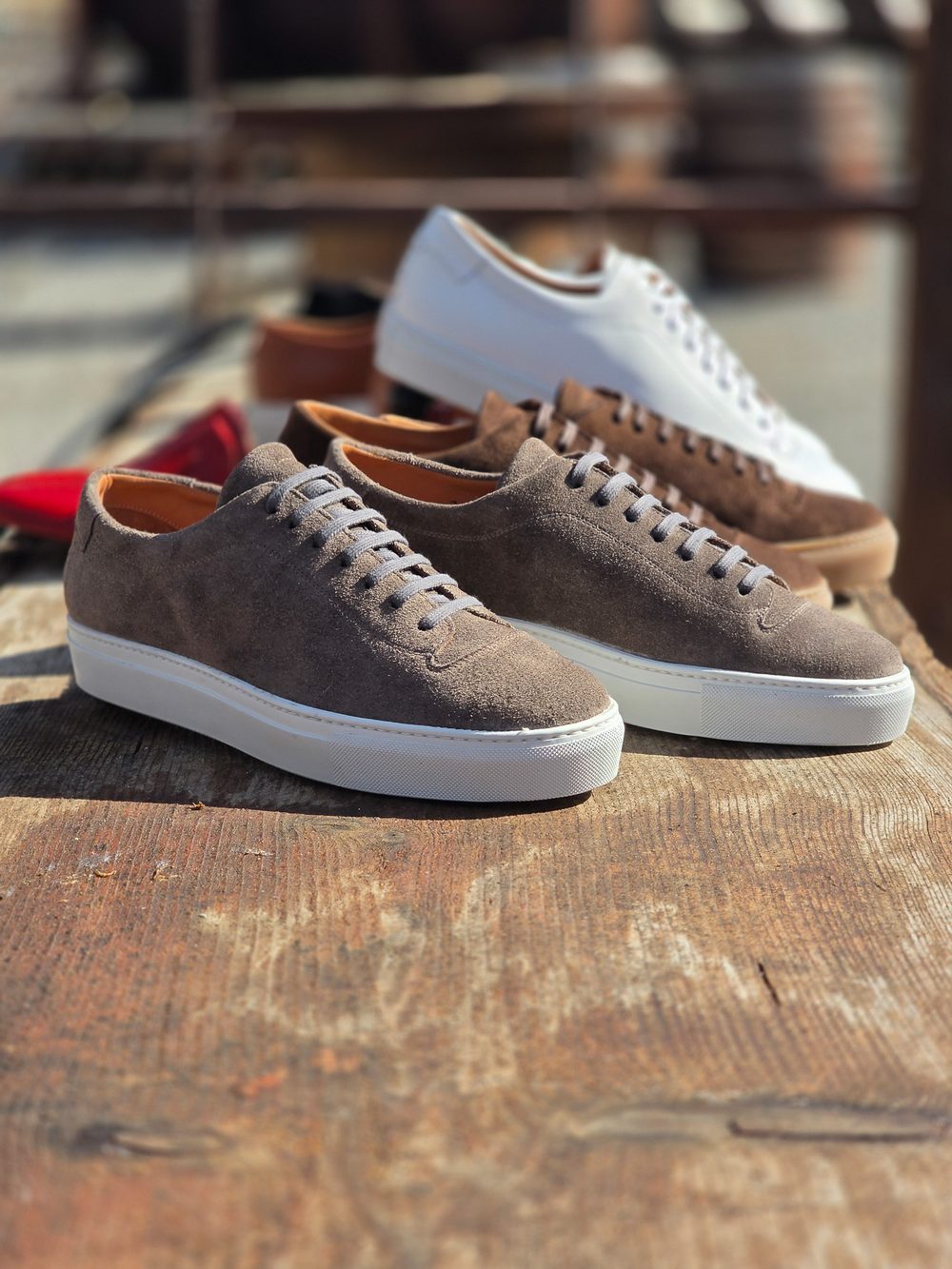 A pair of brown suede sneakers with white soles, placed alongside other colored sneakers.