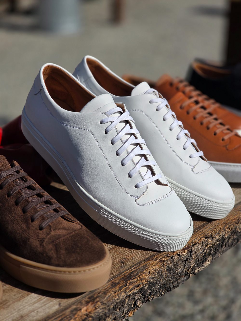 A pair of white leather sneakers with white laces, placed next to brown suede sneakers on a wooden surface.