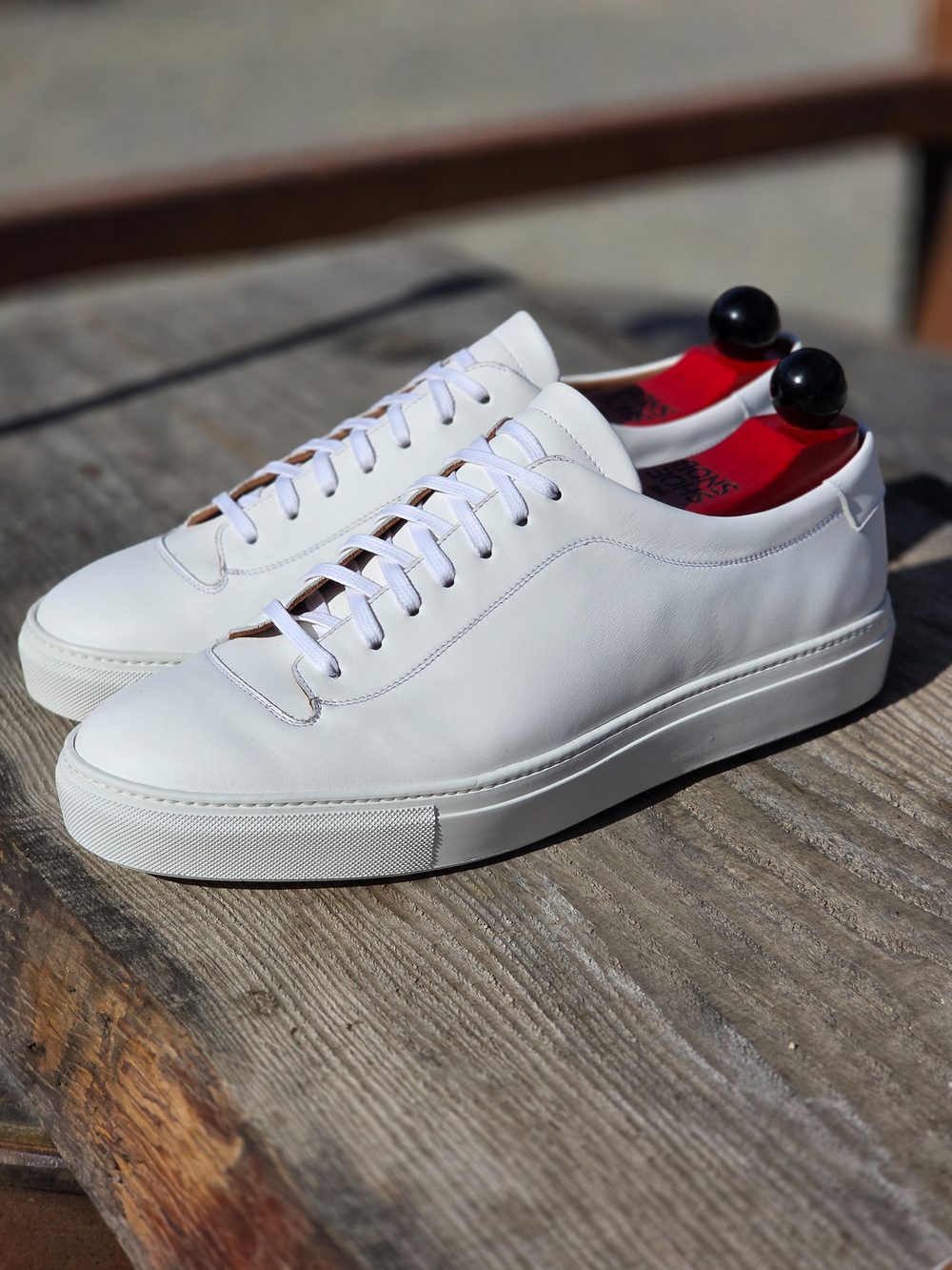 A pair of white leather sneakers with white laces and red insoles.