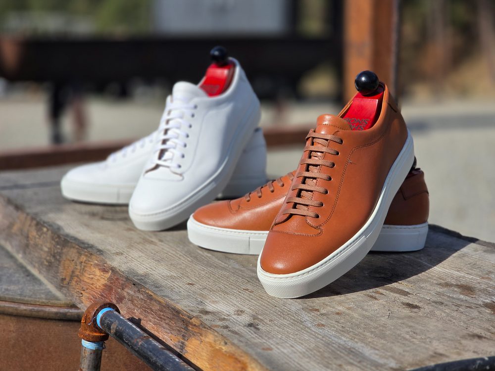 Two pairs of sneakers, one white and one brown, displayed on a wooden surface.