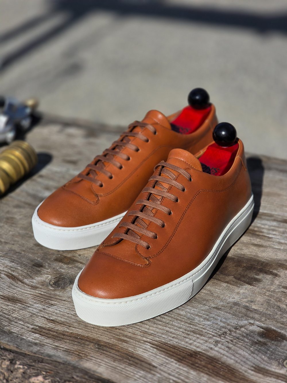 A pair of brown leather sneakers with a white sole and red insoles.
