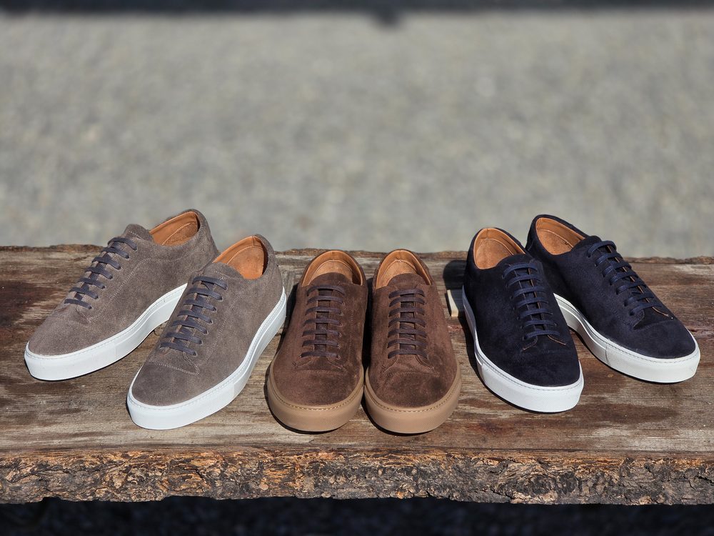 Three pairs of suede sneakers in light gray, brown, and navy, each with white soles and brown insoles.