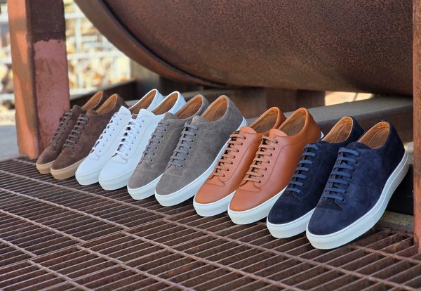 A row of sneakers in various colors, including brown, white, gray, tan, and navy, displayed on a metal grate.