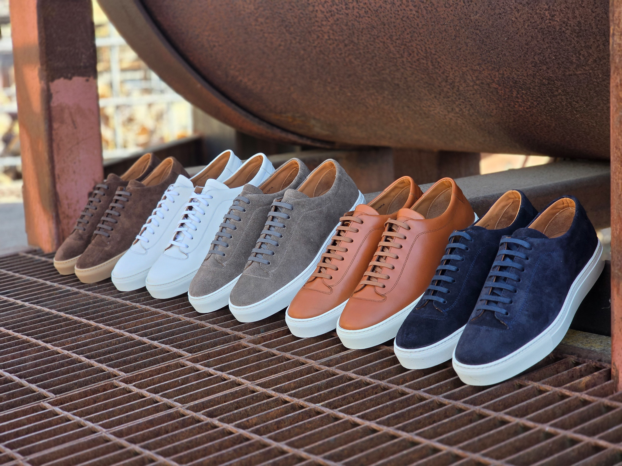 A row of sneakers in various colors, including brown, white, gray, tan, and navy, displayed on a metal grate.