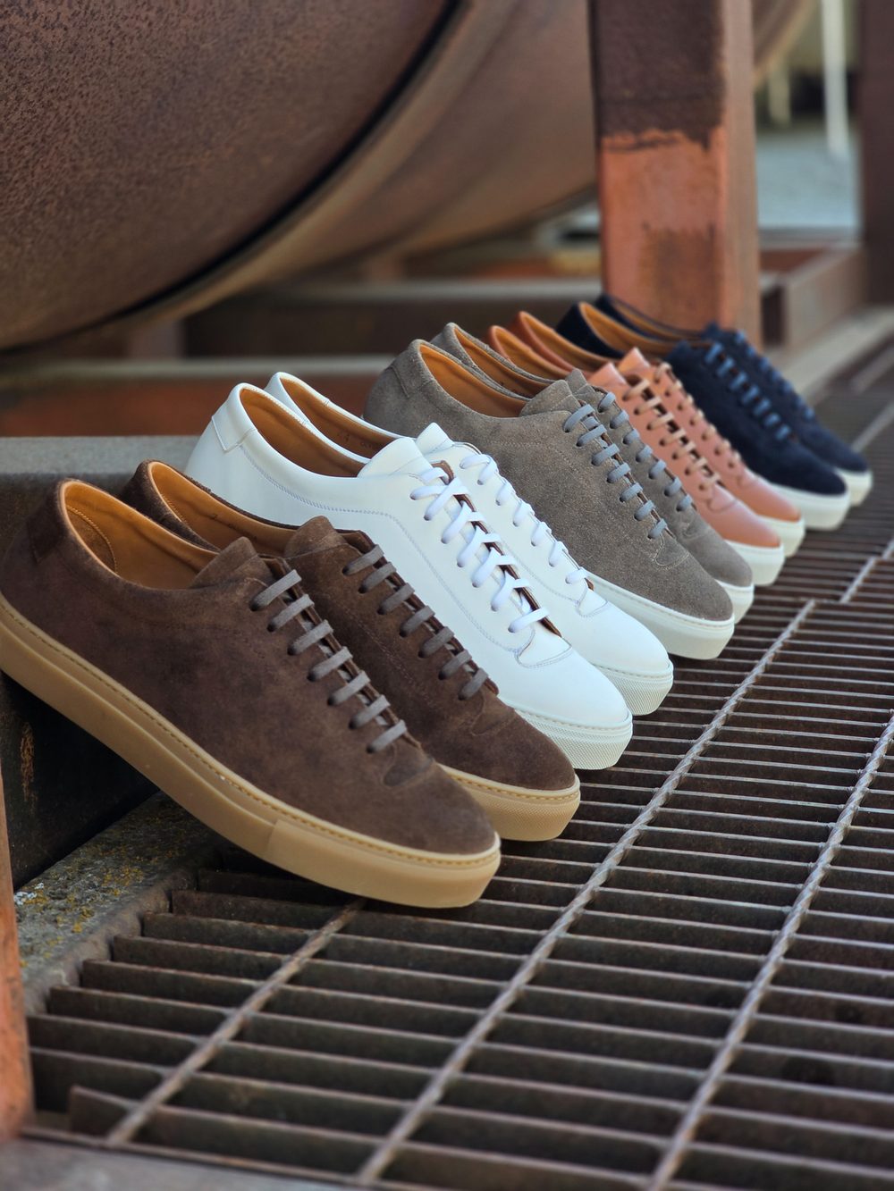 A row of suede sneakers in various colors, including brown, white, pink, and navy, displayed with tan insoles.