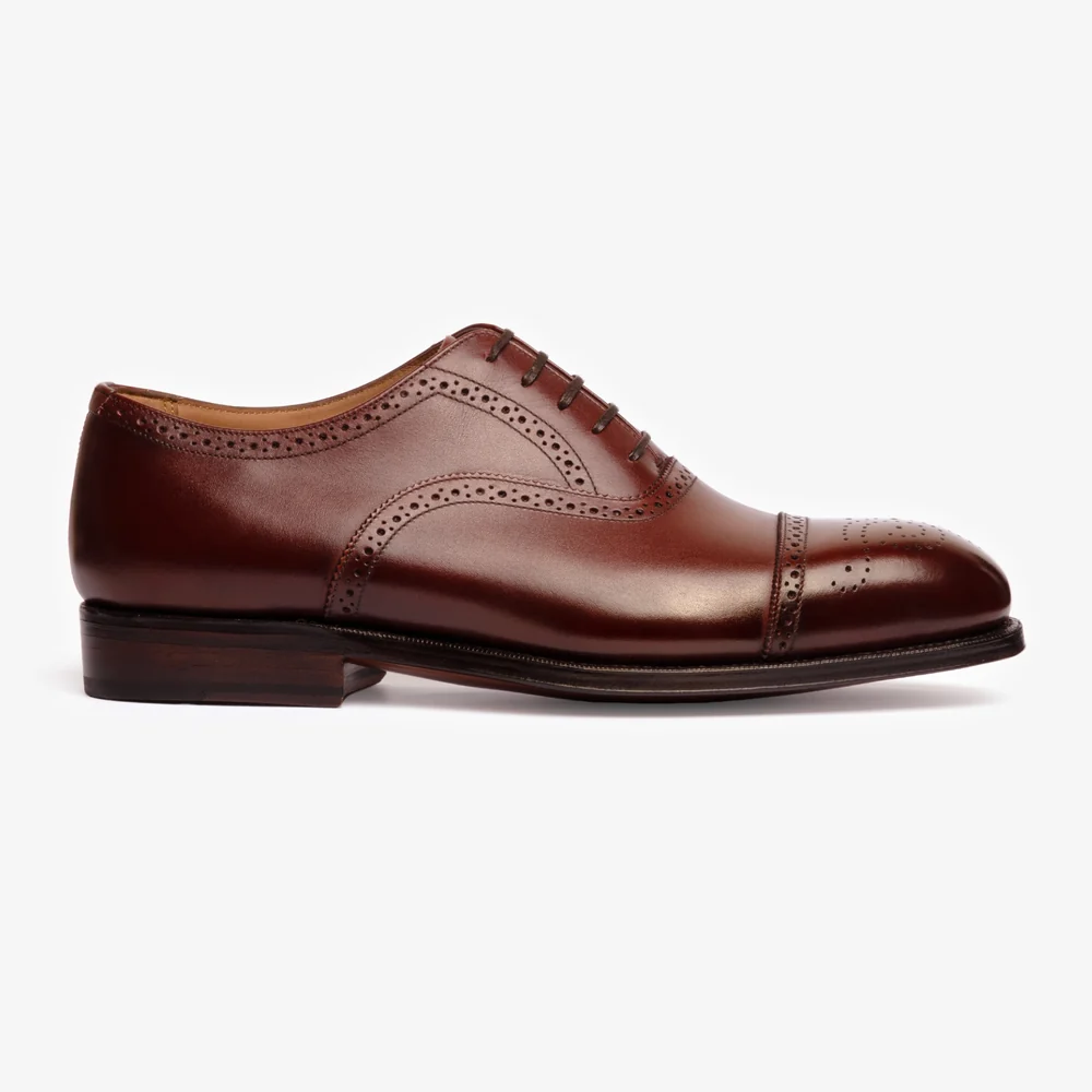 A side view of a polished burgundy leather dress shoe with decorative perforations and a low heel.