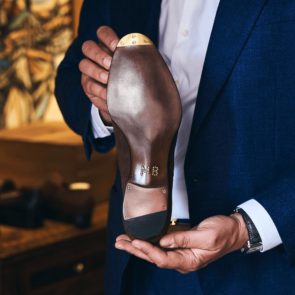 A person holds a brown leather shoe sole featuring a gold toe cap and decorative studs.