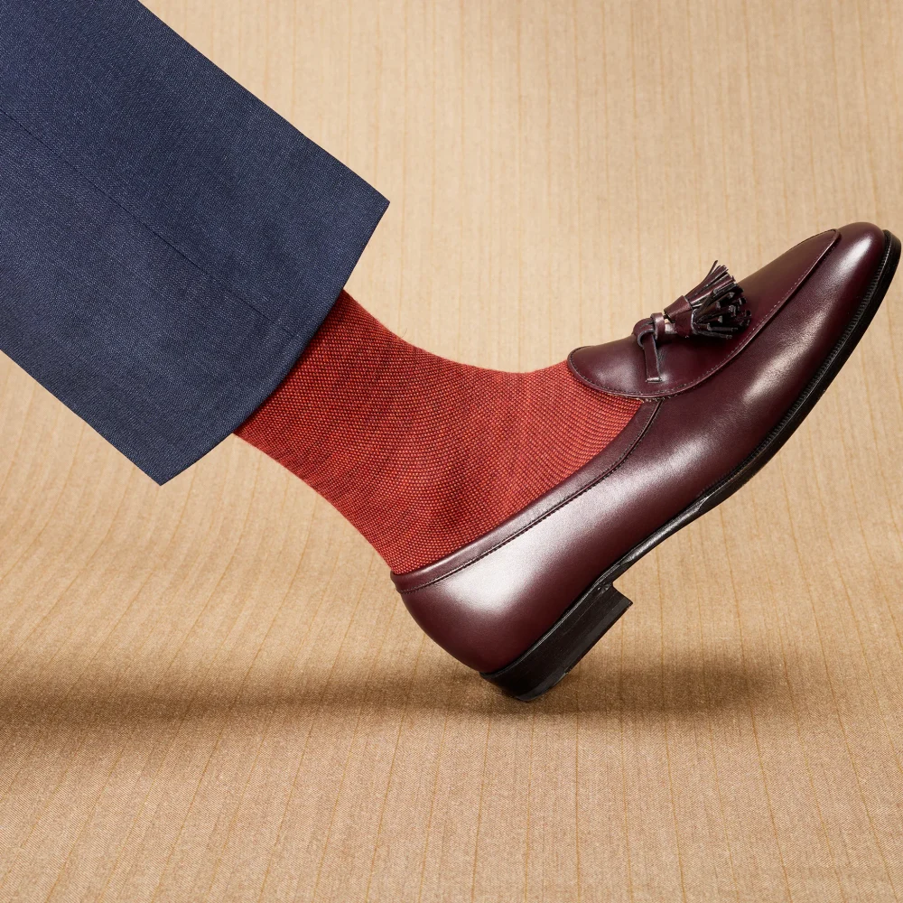 A foot wearing a burgundy over-the-calf sock and a dark leather loafer, with a navy suit pant leg visible.