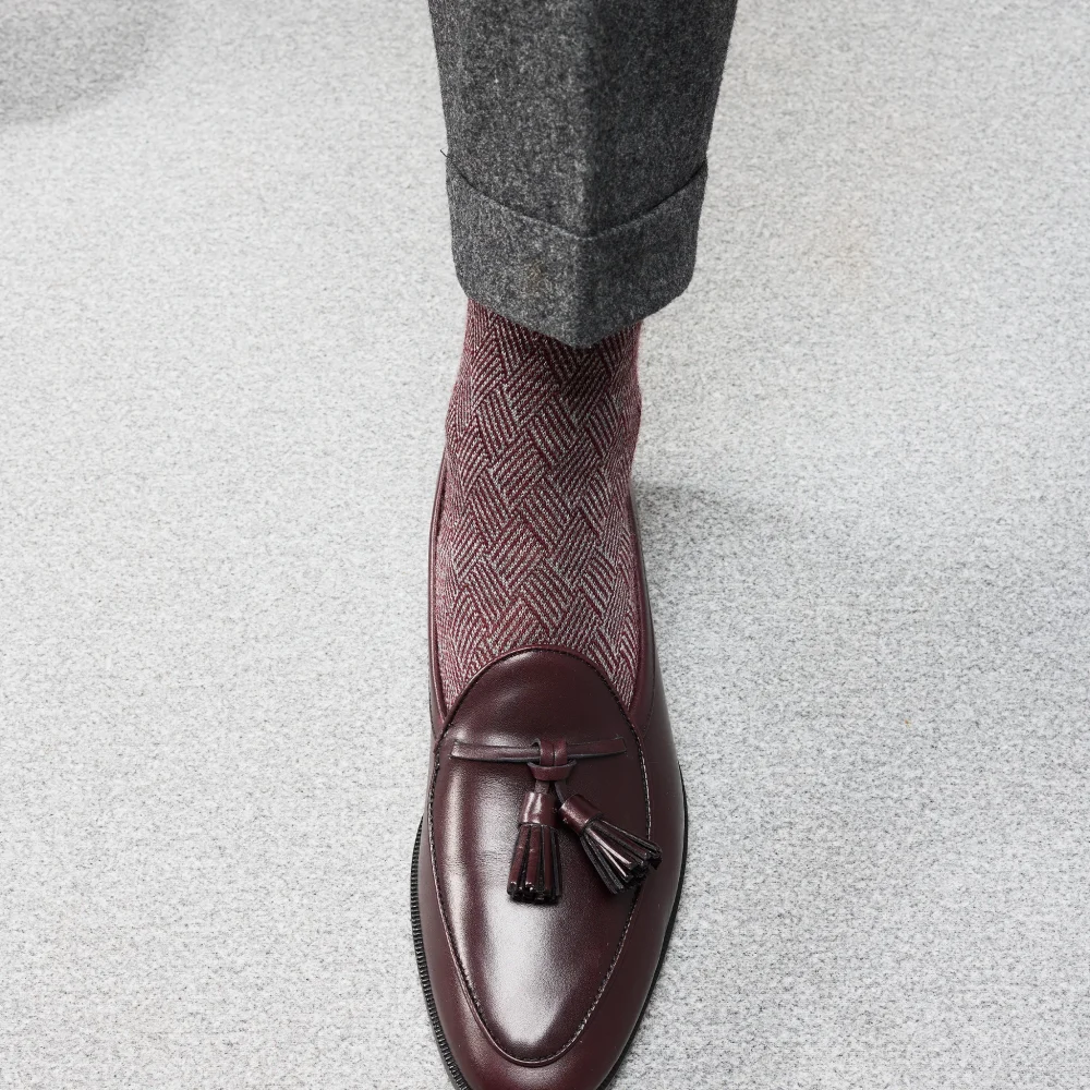 A close-up of a burgundy leather loafer paired with a patterned maroon sock, illustrating over the calf vs mid calf socks.