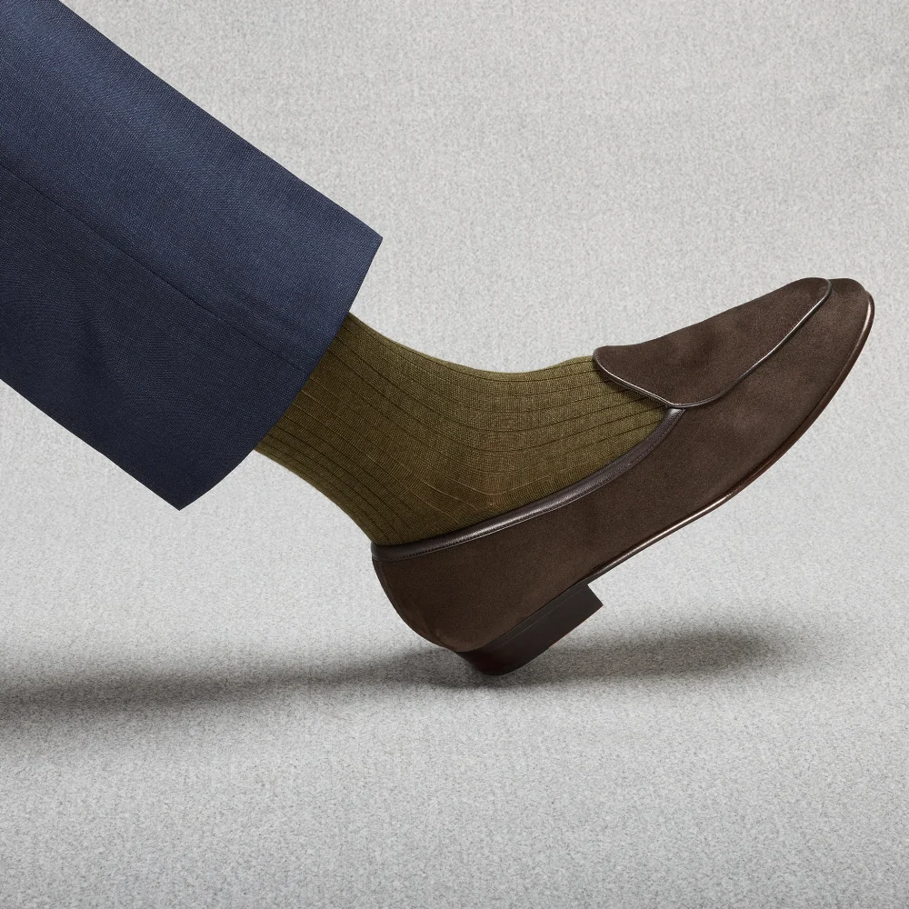 A brown shoe with a folded flap is paired with olive green ribbed socks, illustrating the over the calf vs mid calf socks comparison.