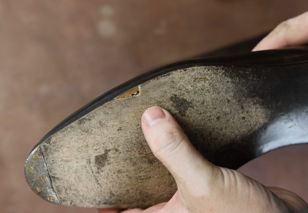 A hand holds a worn leather shoe sole with a visible crack and rough texture.