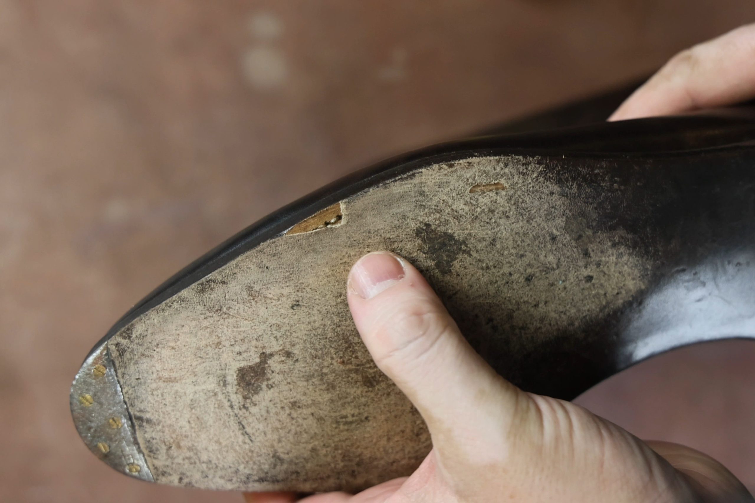 A hand holds a worn leather shoe sole with a visible crack and rough texture.