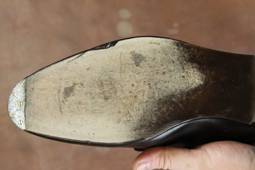 A close-up of a worn leather shoe sole with a smooth dark brown finish and visible scuffs.