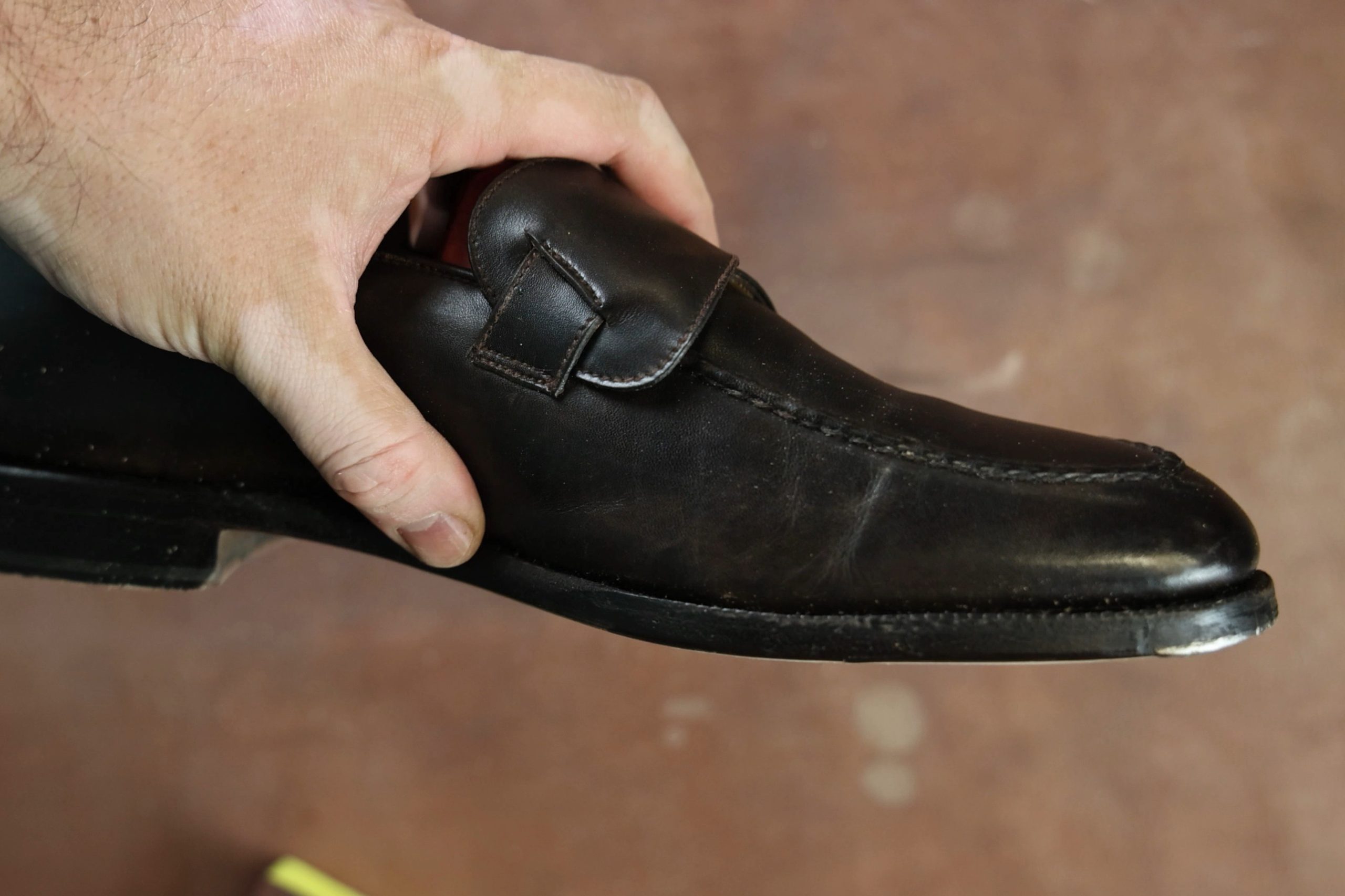 A hand holds a black leather shoe with a closed-channel sole.