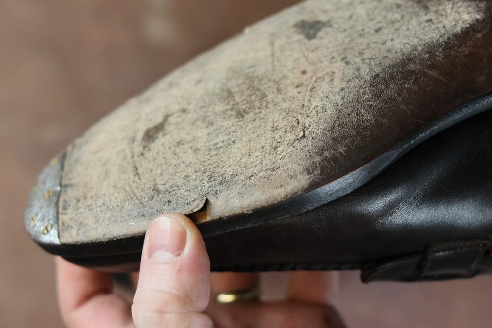 A hand holds a damaged leather shoe sole showing a wear mark and a slight tear.