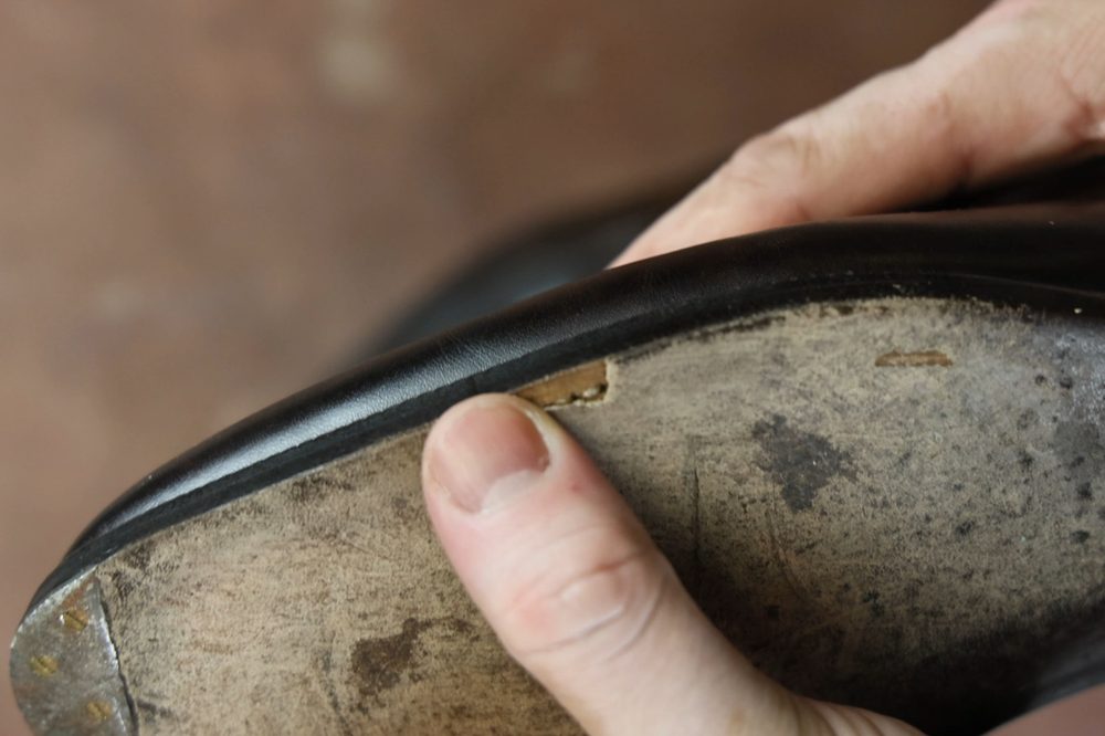 A person’s finger is holding a damaged closed-channel leather sole, showing a crack in the black leather.