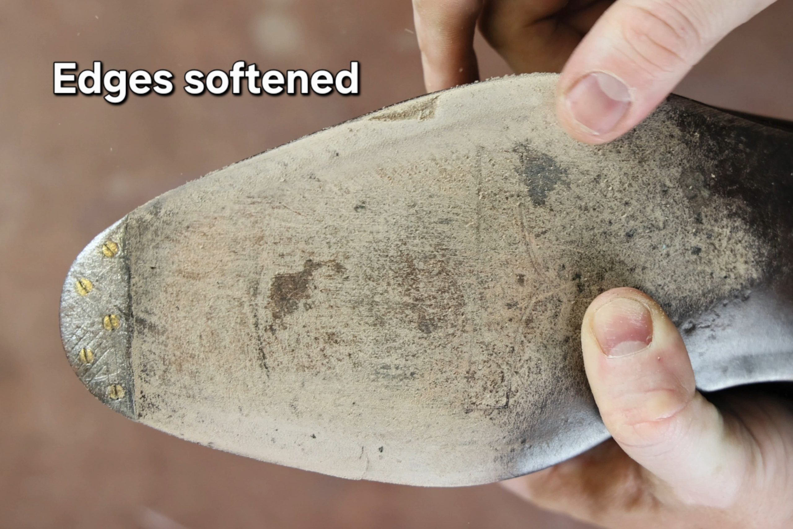 A person holds a worn leather shoe sole with softened edges and visible stitching.