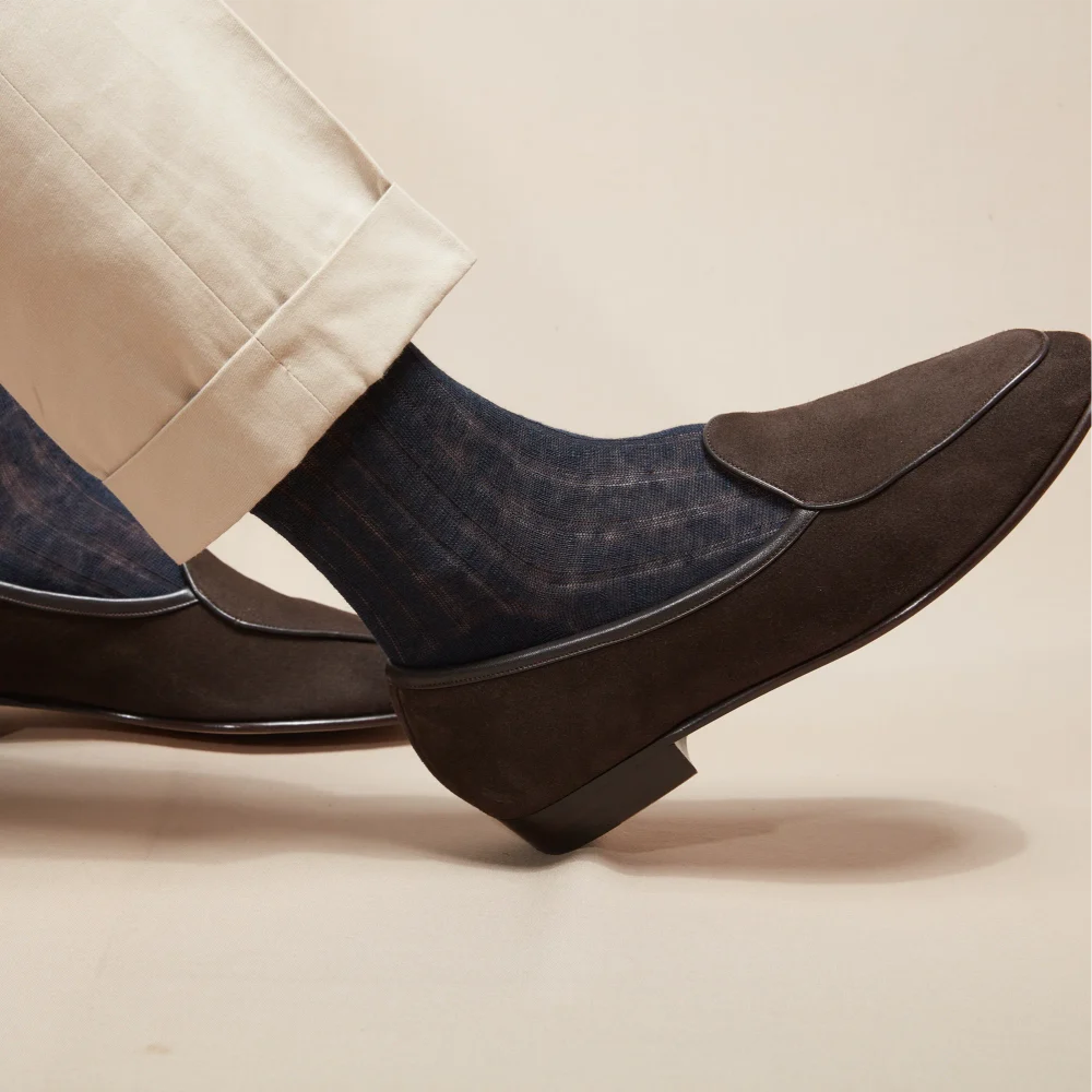 A close-up of a foot wearing a dark blue patterned sock and a brown suede shoe, illustrating the comparison of over the calf vs mid calf socks.