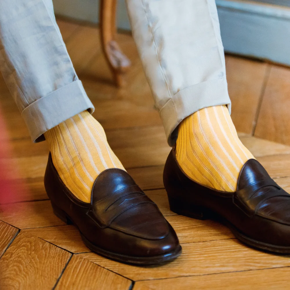A close-up of brown loafers paired with yellow striped mid-calf socks, illustrating the style difference in over the calf vs mid calf socks.