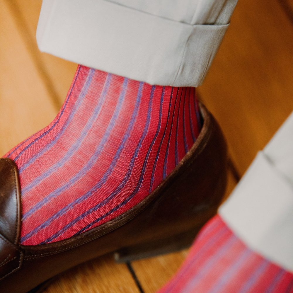 A close-up of a foot wearing red and blue striped over-the-calf socks paired with a brown shoe.
