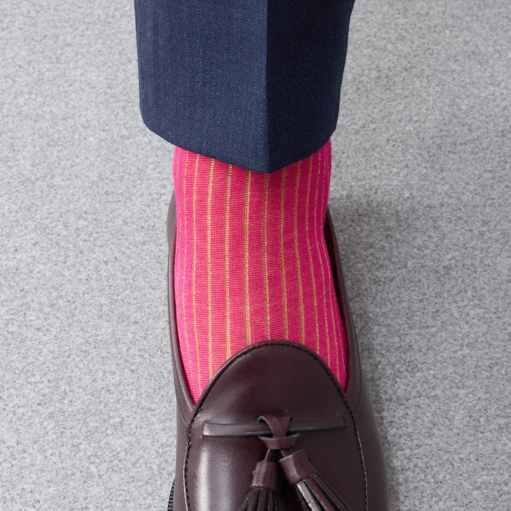 A close-up of a foot wearing bright pink striped over-the-calf socks and a brown leather loafer.