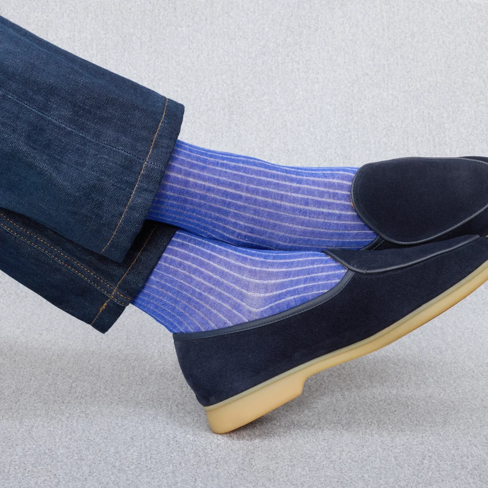 A close-up of blue striped socks worn with dark shoes and denim pants, illustrating the comparison of over the calf vs mid calf socks.