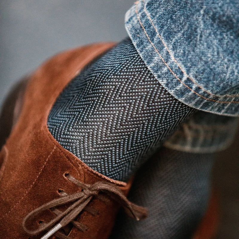 A close-up of a brown suede shoe paired with a herringbone-patterned sock, illustrating the difference between over the calf vs mid calf socks.