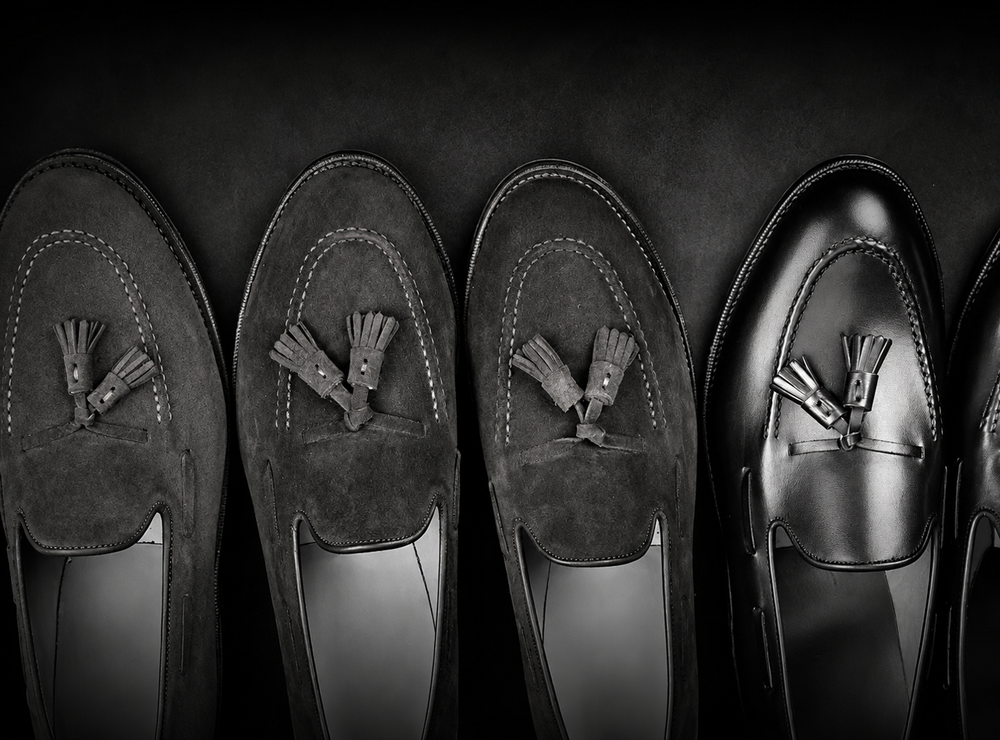 Three pairs of loafers in dark suede and black leather, featuring decorative tassels on the front.