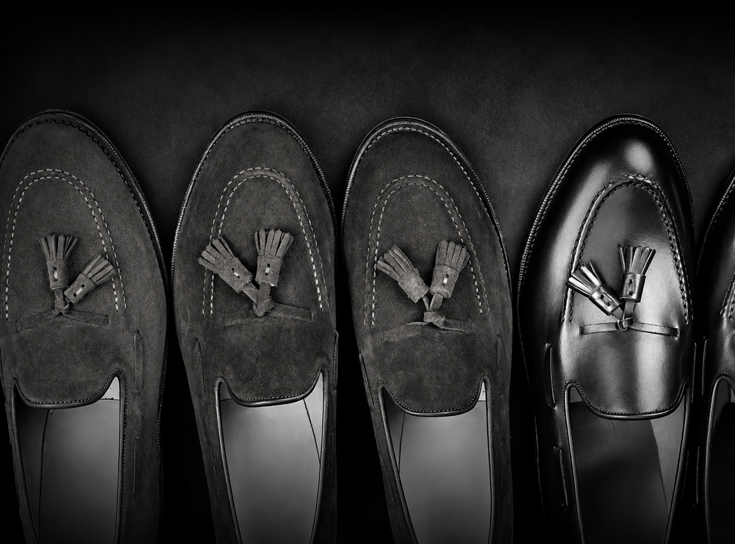 Three pairs of loafers in dark suede and black leather, featuring decorative tassels on the front.
