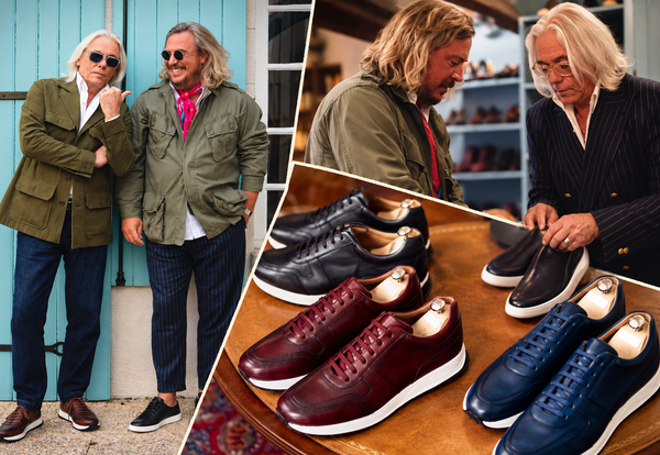 Two men in stylish jackets stand next to a display of sartorial sneakers in dark colors, including burgundy and navy.